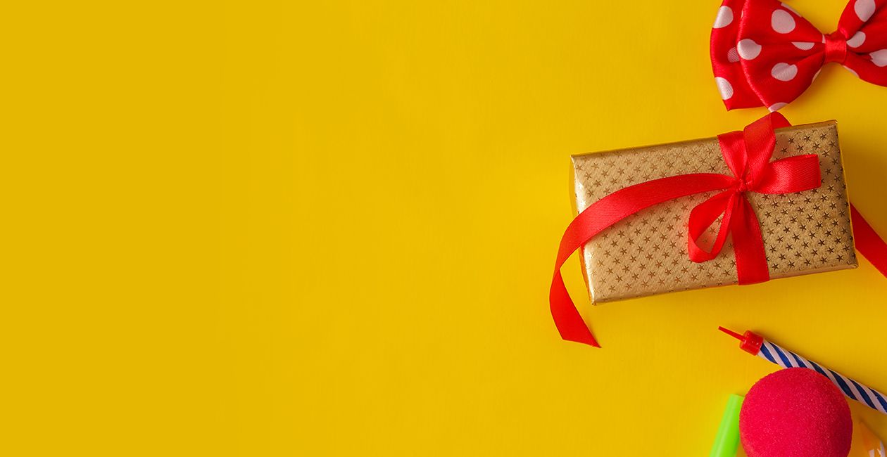 a wrapped present with a red ribbon, a red bow tie, streams and pink ribbon on a yellow background