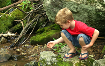 Boy in red shirt and shorts standing on a rock by the river