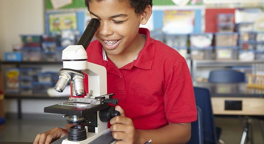 Boy in red shirt looking though a microscope in a classroom