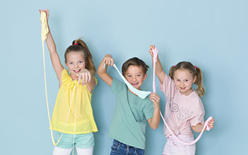 two girls and one boy playing with a lot of slime in front of blue background and having a lot of fun