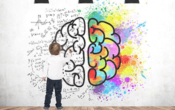 Boy writing formulas on a white wall with a brain and color splashes on it.