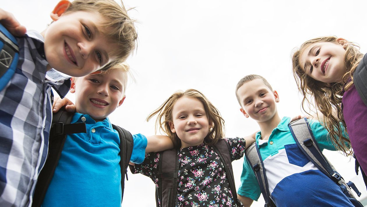 Kids looking down with arms around each all wearing school bags