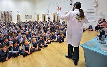 Young students sitting on the gym floor watching a Mad Science special event